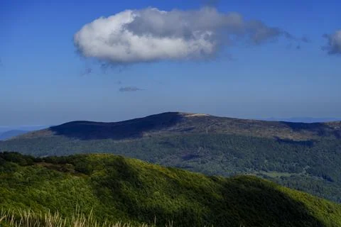Lonely cloud drifting above forested mountain ridges in deep blue sky Stock Photos