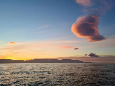 Lonely cloud over the sea in rays of setting sun over the mountains of the is Stock Photos