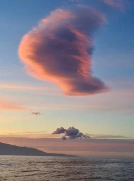 Lonely cloud over the sea in rays of setting sun over the mountains of the is Stock Photos