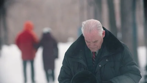 A lonely elderly man standing in the snowy park and looking in the camera Stock Footage 125413601