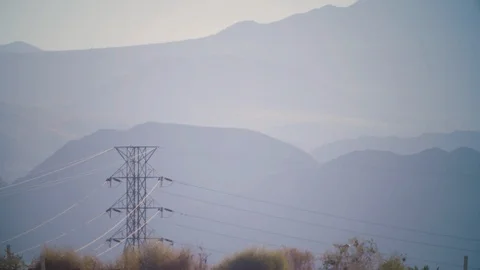 Lonely electrical line infrastructure hovers below desert mountains, California Stock Footage 113290346
