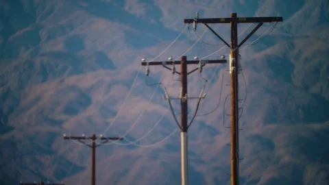 Lonely electrical line infrastructure hovers below desert mountains, California Stock Footage 113290885