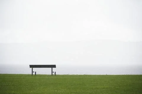 Lonely empty bench in open tranquil landscape by the sea for mindfulness and Stock Photos
