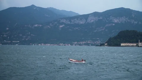 Lonely fisher boat on lake with rough waves and mountains, 4K Stock Footage