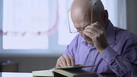 Lonely gray haired man with glasses reading book sitting at table Stock Footage 164929578