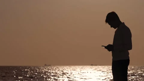 Lonely guy by the sea at sunset scrolling the phone keypad to check messages Stock-Footage 227520877