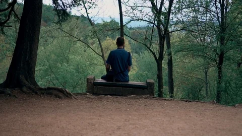 Lonely guy sitting on a bench in the woods Stock Footage 107846785