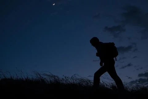 Lonely man with backpack during night outdoors hiking in hills with blowing wind Stock Photos
