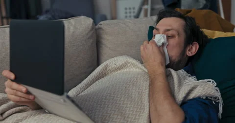 Lonely man with beard and black hair is lying on sofa and covered with blanket 動画素材 218322995