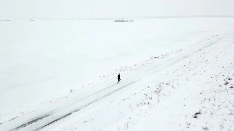 A lonely man in black tracksuit is running along a snowy road. Winter, around Stock Footage 101713527