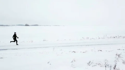 A lonely man in black tracksuit is running along a snowy road. Winter, around Stock Footage 101714190