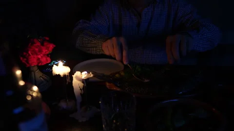 Lonely man eats baked carp fish with vegetables by candlelight at night time Stock Footage 282696201