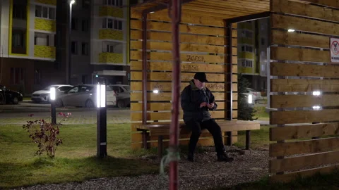A lonely man in the evening sits on a bench and uses a smartphone in cold Stock Footage 142268003