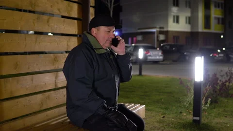 A lonely man in the evening sits on a bench and talks on the phone in cold Stock Footage 142269706