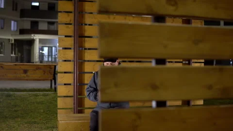 A lonely man in the evening sits on a bench and uses a smartphone in cold Stock Footage 142270365