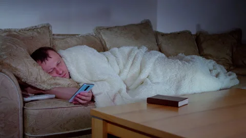 A lonely man lies on the sofa in front of the television at night with his Stock Footage 318314746