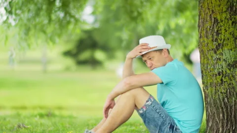 Lonely man resting in the shade of a tree while sitting in the park, side view Stock Footage 148964121