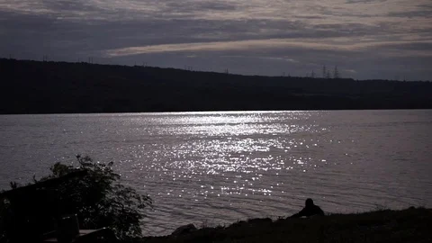 Lonely man by the river, sunset, rays reflect on the water Stock Footage 114630976
