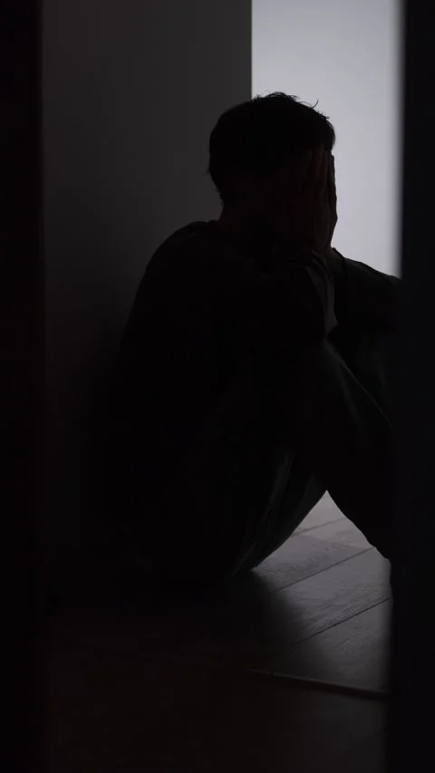 Lonely man silhouette sitting on floor in dark corridor with light doorway Stock Footage 325074009