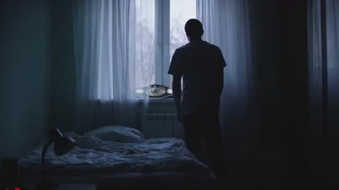 Lonely Man Silhouette Standing by Window with Curtains in Dark Bedroom Stock-Footage 331774194