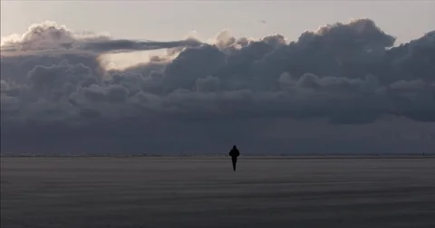 Lonely man walking at the beach with epic clouds and sand blowing Stock Footage 83873129