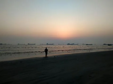 Lonely Man Walking on a Beach at Sunset with Ships in the Horizon Stock Photos