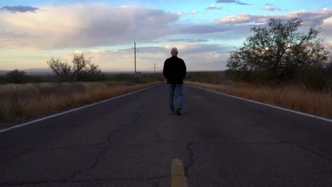 A lonely man walking down the center of a country road Stock Footage 294727101