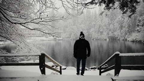 A lonely man walking towards partly frozen, mountain lake of Swiss Stock Footage 224744312