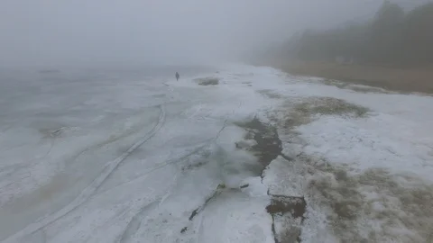 Lonely man walks through snow and ice of frozen sea coastline 動画素材 91795375