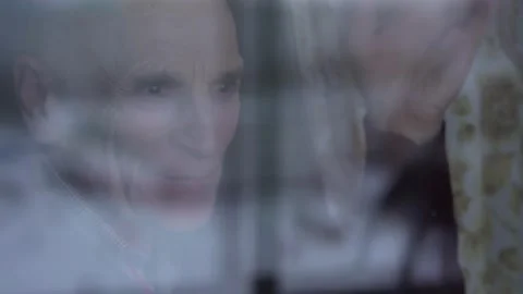 Lonely oldster standing behind window glass and waving with hand Video stock 169749696