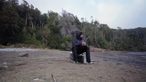 Lonely person sitting on log drinking mate on exotic beach in winter Stock Footage 314045340