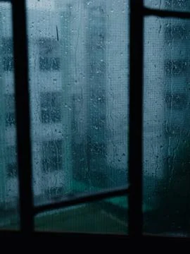Lonely Rainy Window View of Distant City Building in Dim Blue-Teal Light, M.. Foto stock