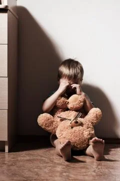 Lonely sad boy crying in corner, holding toy bear Stock Photos