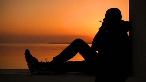 Lonely sad guy smokes at sunset by the sea 库存影片 150281562