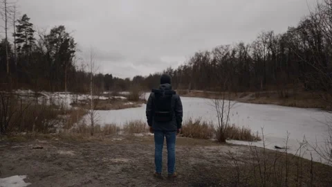Lonely sad man, standing with his back and looking at frozen lake inforest Stock Footage 150664700