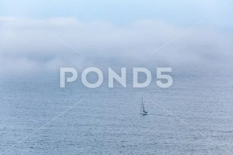 Lonely sailboat sailing the vast ocean under low clouds with copy space Stock Photos