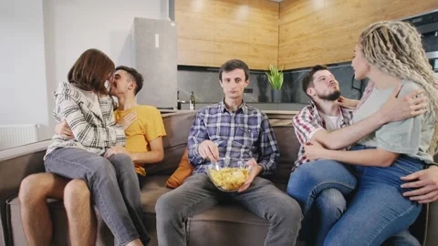 Lonely single man sitting on sofa and eating chips while watching two loving Stock Footage 278490114