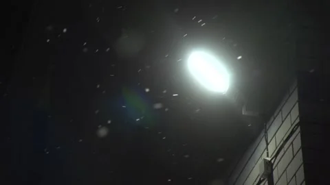 Lonely street light on the wall with light leak in night when windy and snowing Stock Footage 166558027