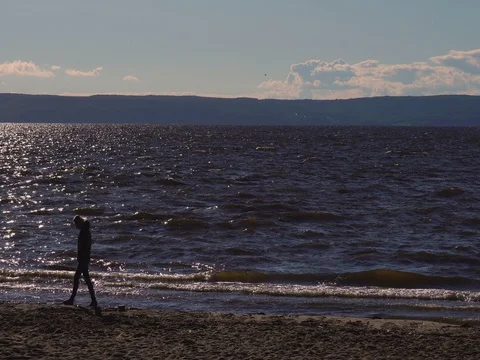 A lonely woman slowly walks along an empty sandy beach Stock Footage