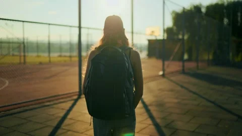 Lonely youth with backpack walking towards metal fence under bright sunlight. 库存影片 339809165