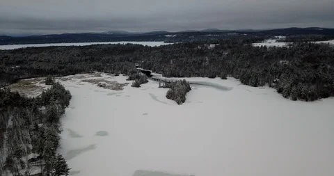 Long aerial shot flying down toward snowy frozen lake and deep forests Stock Footage 124828449