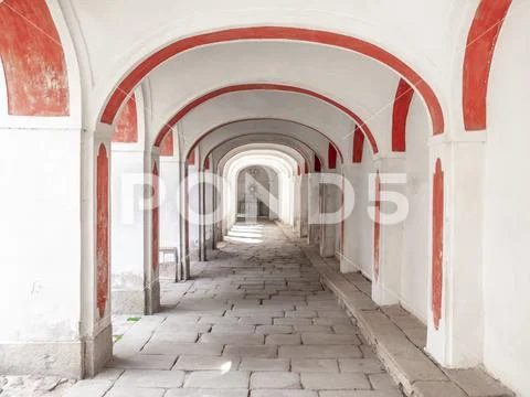 Long arcade corridior with white and red facade and cobbled floor Stock Photos