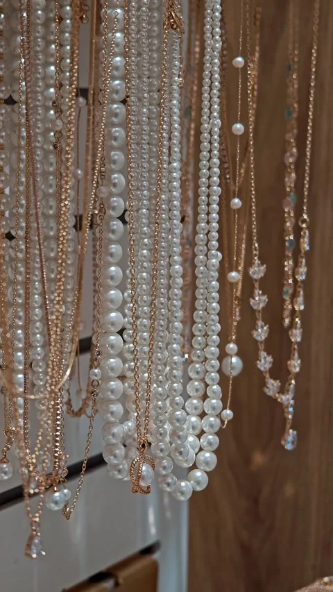 Long artificial white pearl necklaces hanging in store. Classic accessories for Stock Footage 330795989