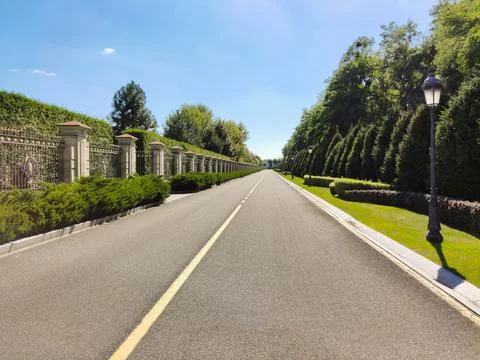 A long asphalt empty road in perspective between a decorated fence and a park Stock Photos