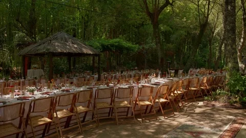 Long banquet table under trees with wooden chairs at forest venue 動画素材 344512199