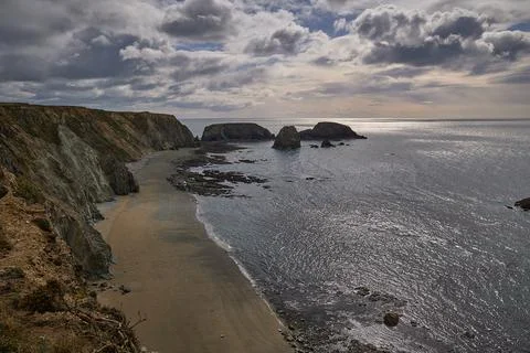 Long beach with cliffs. very cloudy sky and strong sun. Stock Photos