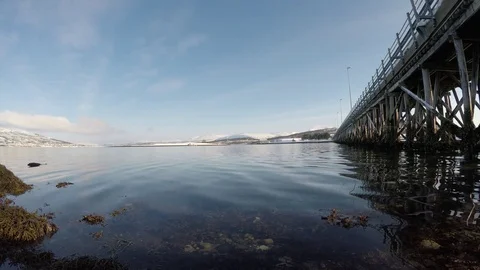 Long beautiful bridge with bright sunshine on blue sky with calm moving waves Stock Footage