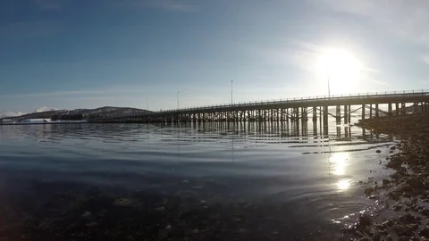 Long beautiful bridge with bright sunshine on blue sky with calm moving waves Stock Footage