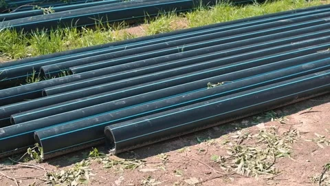 Long black plastic pipes are arranged in neat rows on grassy ground in an Stock Footage 338446707