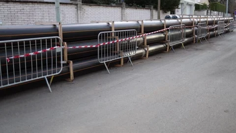 Long black plastic pipes stacked along a residential street, secured with wooden Stock Footage 304885319